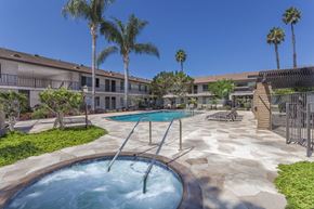 Fountain Valley apartment for rent - A pool with a slide in the middle of a courtyard surrounded by palm trees.