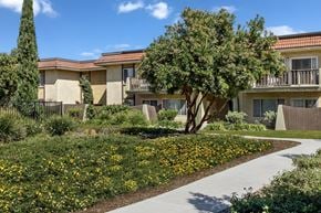 Oxnard apartment for rent - A building with a yellow flower bed in front of it.