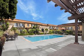 Oceanside apartment for rent - A pool area with a table and chairs and a building in the background.