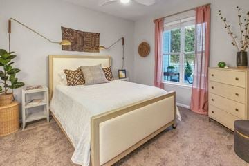 Mooresville apartment for rent - A bedroom with a large bed, a nightstand, and a window with pink curtains.