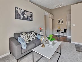 Milford apartment for rent - A living room with a grey couch, a coffee table, and a world map on the wall at The Reserve at Grand Valley Apartments, Milford 46150
