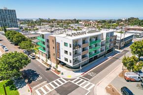 Chula Vista apartment for rent - A modern building with the word "SUNSET" on the side is surrounded by trees and a busy street.
