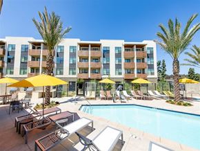 Chula Vista apartment for rent - A pool area with lounge chairs and umbrellas in front of a multi-story apartment building.