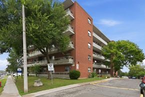 Hamilton apartment for rent - A red brick apartment building with a parking lot in front.