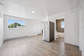 Kitchener apartment for rent - A spacious, empty room with a white fridge and wooden flooring.
