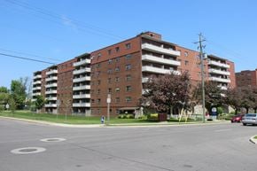Hamilton apartment for rent - A large red brick apartment building with a parking lot in front.