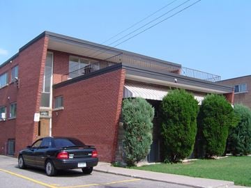 Hamilton apartment for rent - A black car is parked in a parking space in front of a red brick building.