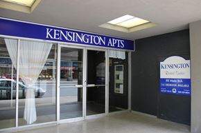Hamilton apartment for rent - The image shows the front of Kensington Apts with a blue signboard and a window with white curtains.