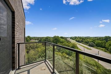 Kitchener apartment for rent - A balcony with a glass railing overlooks a highway and trees.