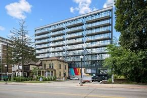 Kitchener apartment for rent - A modern glass building is situated next to a tree and a house.