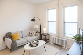 Kitchener apartment for rent - A living room with a grey couch, a white table, and a grey floor lamp.
