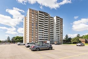 Hamilton apartment for rent - A parking lot with cars and a tall building in the background.