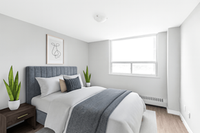 Hamilton apartment for rent - A bedroom with a bed, pillows, a blanket, a nightstand, and a window.