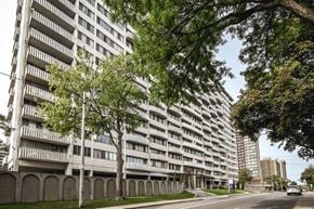 Hamilton apartment for rent - A tall residential building with balconies is surrounded by trees.