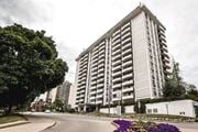 Hamilton apartment for rent - A tall residential building with balconies is surrounded by trees and a street with a flower bed.