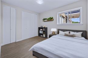 Hamilton apartment for rent - A bedroom with a large bed, a window with a view of a house, and a shelf with books and a plant.