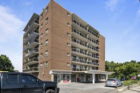 Stoney Creek apartment for rent - A large brick building with a parking lot in front.