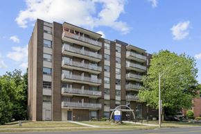 Hamilton apartment for rent - A tall apartment building with balconies and a blue sign in front.