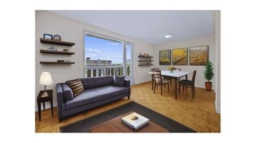 Hamilton apartment for rent - A living room with a grey couch, a small table with a lamp, a dining table with chairs, and pictures on the wall.