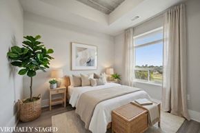 Kitchener apartment for rent - A bedroom with a large bed, a plant, and a window with curtains.