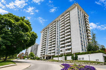 Hamilton apartment for rent - A tall residential building with balconies is surrounded by greenery and a clear blue sky.