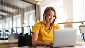 A woman in a yellow shirt is using a laptop