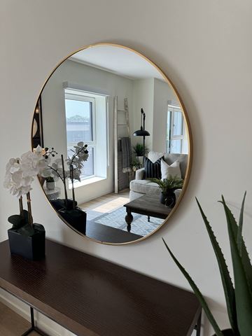 Dundas apartment for rent - A round mirror with a gold frame reflects a living room with a white couch and a black coffee table.