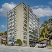 Hamilton apartment for rent - A tall beige building with many windows is surrounded by trees and parked cars.