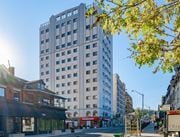 Hamilton apartment for rent - A tall building with many windows stands in the middle of a street.