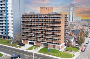 Hamilton apartment for rent - A large apartment building is situated on a street corner with cars parked along the curb.