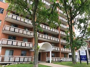 Hamilton apartment for rent - A tall apartment building with balconies and a blue sign in front.