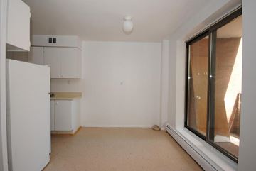Hamilton apartment for rent - A white kitchen with a refrigerator, cabinets, and a window.
