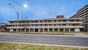 Hamilton apartment for rent - A large building with a red roof and white walls is surrounded by a grassy area and a street.