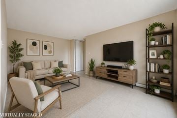 Hamilton apartment for rent - A living room with a white chair, a brown couch, a glass coffee table, a flat screen TV, and a bookshelf with plants.