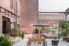 Newburgh apartment for rent - A man is sitting on a bench under a blue umbrella in a courtyard with plants and flowers.