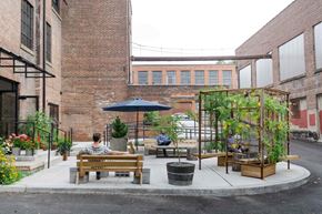 Newburgh apartment for rent - A person is sitting on a bench under a blue umbrella in a courtyard with plants and a trellis.
