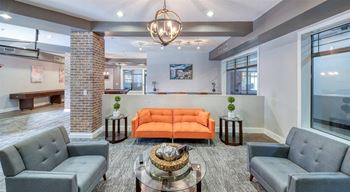 Clubhouse with grey chairs, an orange sofa, and a glass coffee table