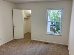 Virginia Beach townhouse for rent - A room with a carpeted floor, a white door, and a window with a view of trees and a house outside.