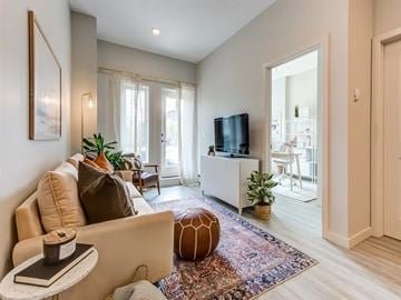Edmonton apartment for rent - A living room with a beige couch, a small table with a book and a candle, a television, and a rug with a pattern.