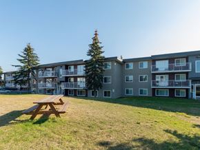 Prince George apartment for rent - A wooden picnic table is in the foreground of a grassy area in front of apartment buildings.