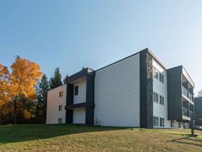 Prince George apartment for rent - A modern building with a white and black facade is surrounded by a grassy area and trees.