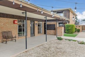 Carlsbad apartment for rent - A building with a red sign on the left side and a bench under a canopy.