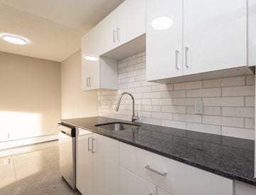 Edmonton apartment for rent - A kitchen with white cabinets and black countertops.