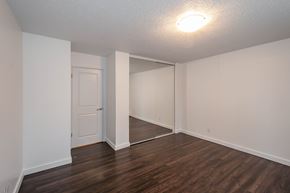 Edmonton apartment for rent - A room with white walls and wooden flooring with a door on the left and a mirror on the right.