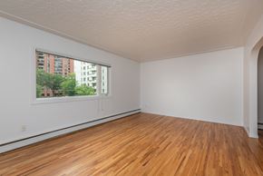 Edmonton apartment for rent - A room with wooden floors and a window showing a view of a building outside.