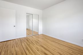 Edmonton apartment for rent - A room with a wooden floor and a white wall with a door and a mirror.