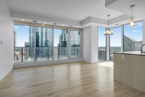 Edmonton apartment for rent - A spacious room with wooden floors and large windows overlooking a cityscape.