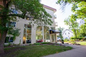 Edmonton apartment for rent - A building with a red awning is surrounded by trees and grass.