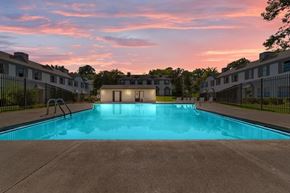 Shreveport apartment for rent - A swimming pool in front of a building with a sunset in the background.