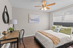 Shreveport apartment for rent - A bedroom with a bed, a table, a chair, a ceiling fan, and a painting on the wall.